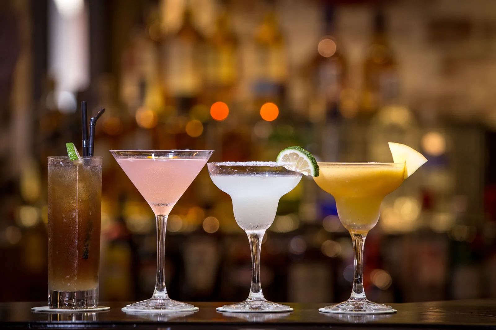 Vibrant cocktails lined up beautifully on a bar counter with a blurred background.